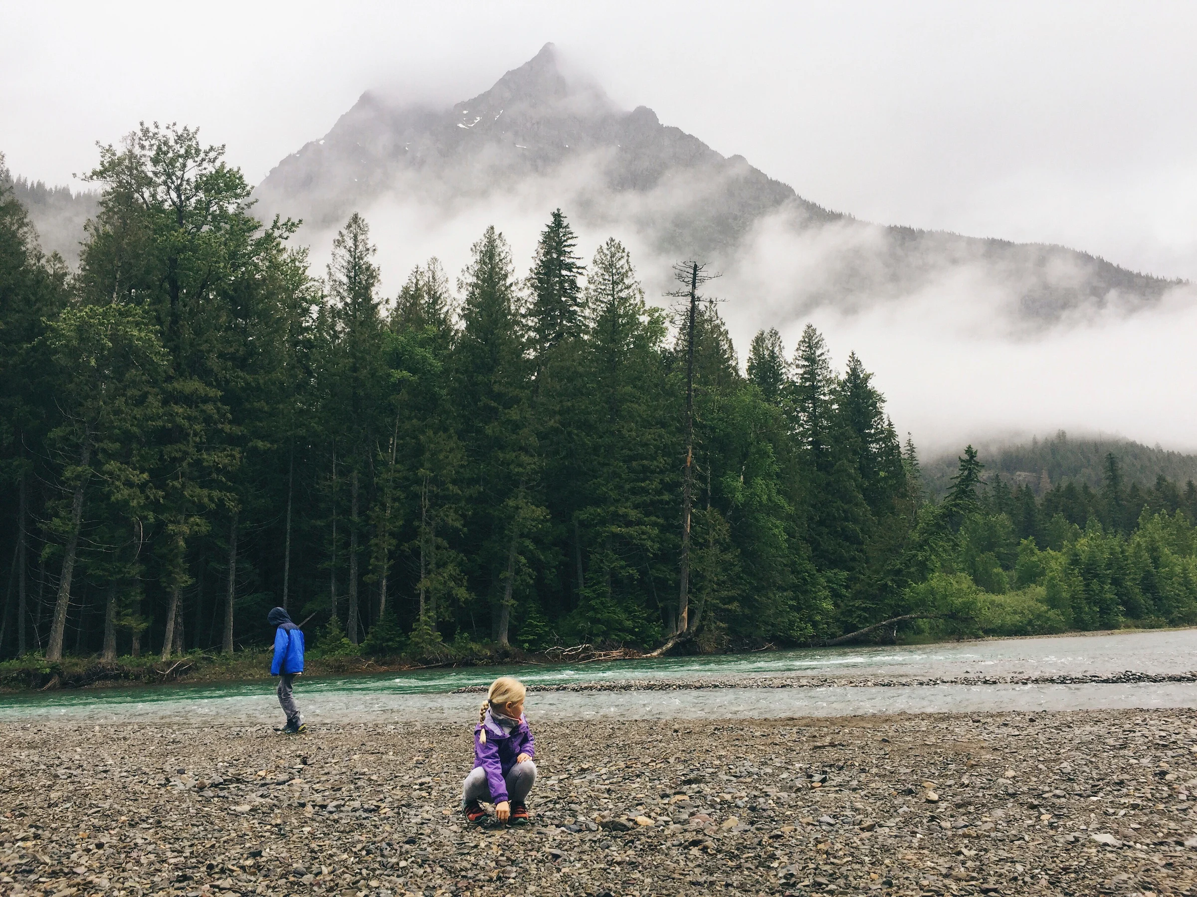 A young girl finds a stone with a mountain in the background.